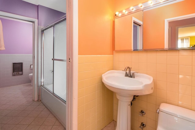 full bath with wainscoting, tile patterned floors, toilet, tile walls, and combined bath / shower with glass door