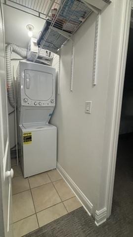 clothes washing area featuring light tile patterned floors, stacked washer / drying machine, baseboards, and laundry area