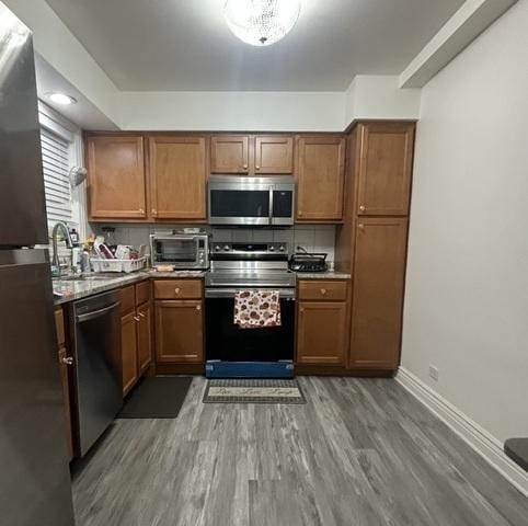 kitchen featuring decorative backsplash, wood finished floors, brown cabinets, and appliances with stainless steel finishes