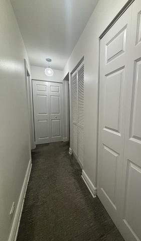 hallway featuring baseboards and dark carpet