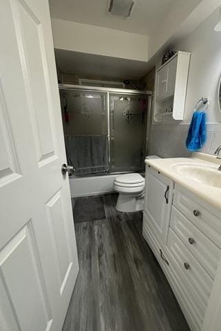bathroom featuring bath / shower combo with glass door, toilet, vanity, and wood finished floors