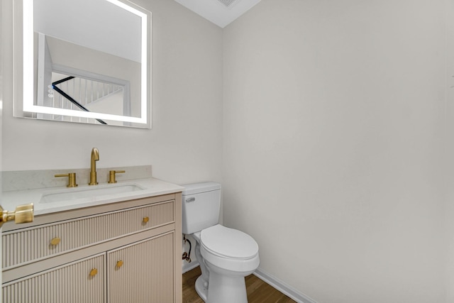 half bath with toilet, baseboards, wood finished floors, and vanity