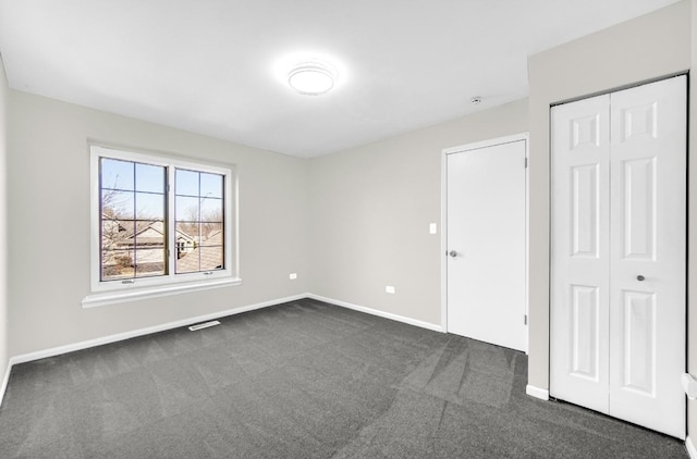 unfurnished bedroom featuring a closet, dark carpet, visible vents, and baseboards