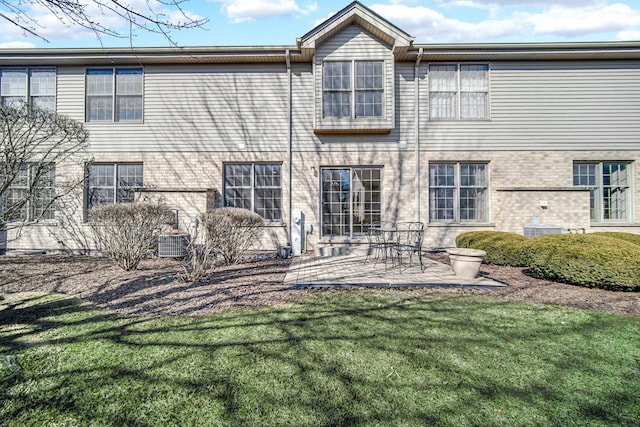 rear view of house with central air condition unit, a patio, a lawn, and brick siding