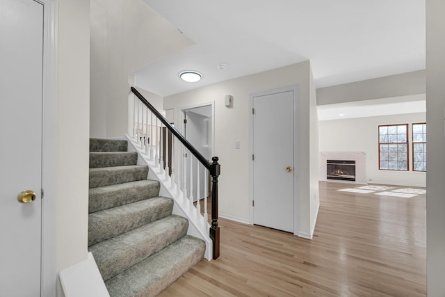 stairs featuring baseboards, wood finished floors, and a high end fireplace