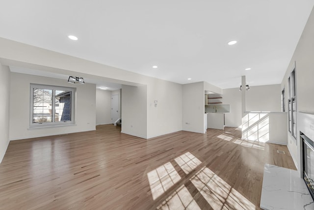 unfurnished living room featuring light wood-style flooring, baseboards, a fireplace with flush hearth, and recessed lighting