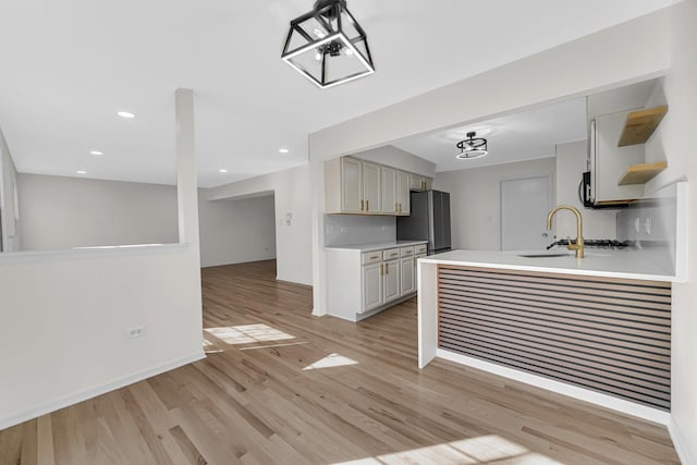 kitchen with a sink, light wood-style floors, light countertops, freestanding refrigerator, and open shelves