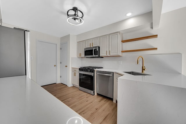 kitchen featuring appliances with stainless steel finishes, light countertops, light wood-style floors, open shelves, and a sink