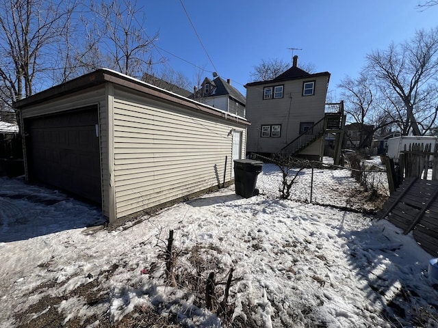 view of snowy exterior with an outbuilding, stairway, a detached garage, and fence