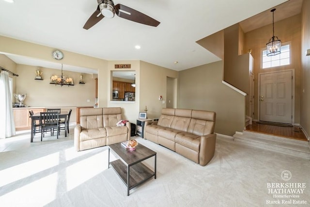 living room featuring light colored carpet, ceiling fan with notable chandelier, and baseboards