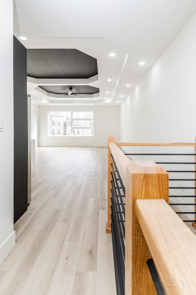 hallway featuring recessed lighting, a raised ceiling, light wood finished floors, and an upstairs landing