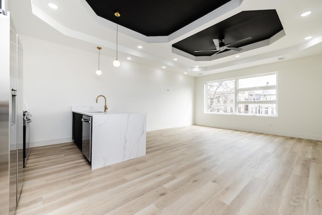 kitchen with a sink, appliances with stainless steel finishes, a raised ceiling, and light wood-style floors