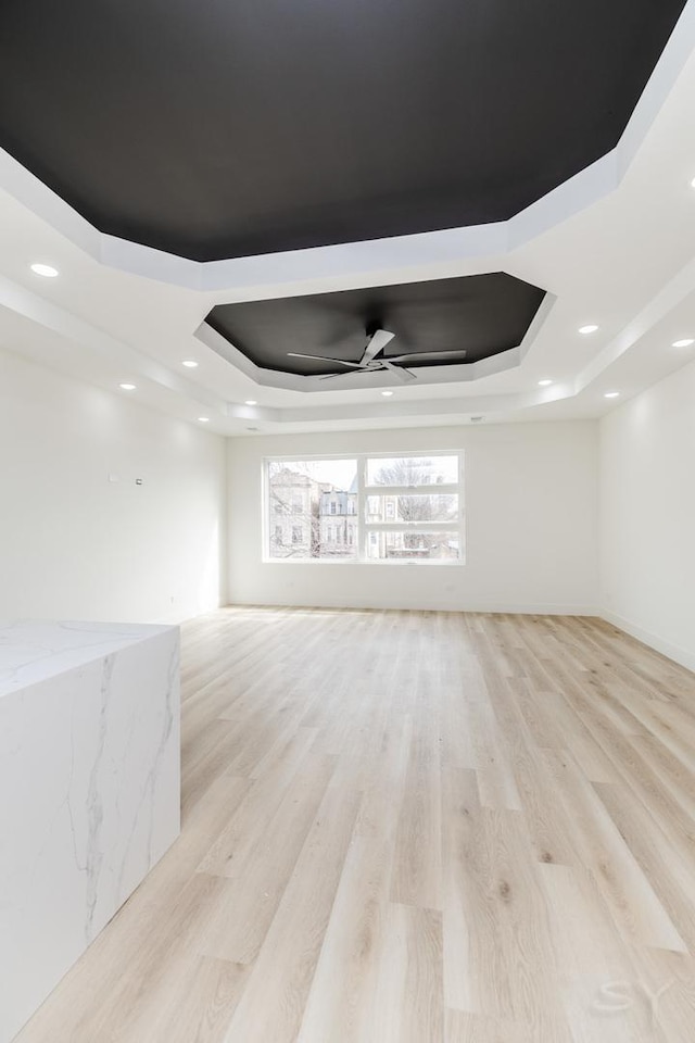 empty room featuring light wood-type flooring, a tray ceiling, ceiling fan, and recessed lighting