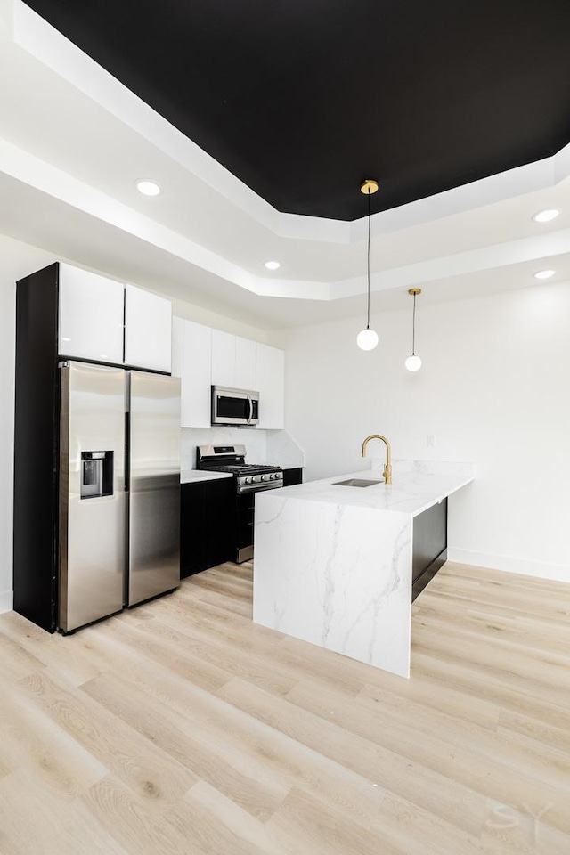 kitchen featuring a raised ceiling, appliances with stainless steel finishes, a peninsula, light wood-style floors, and a sink