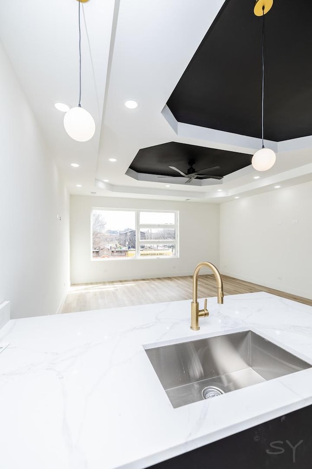 interior details featuring dark cabinets, decorative light fixtures, light stone countertops, a tray ceiling, and a sink