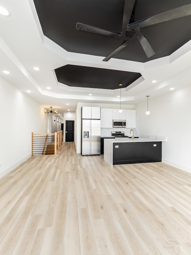 kitchen with appliances with stainless steel finishes, a tray ceiling, white cabinetry, and light wood-style floors