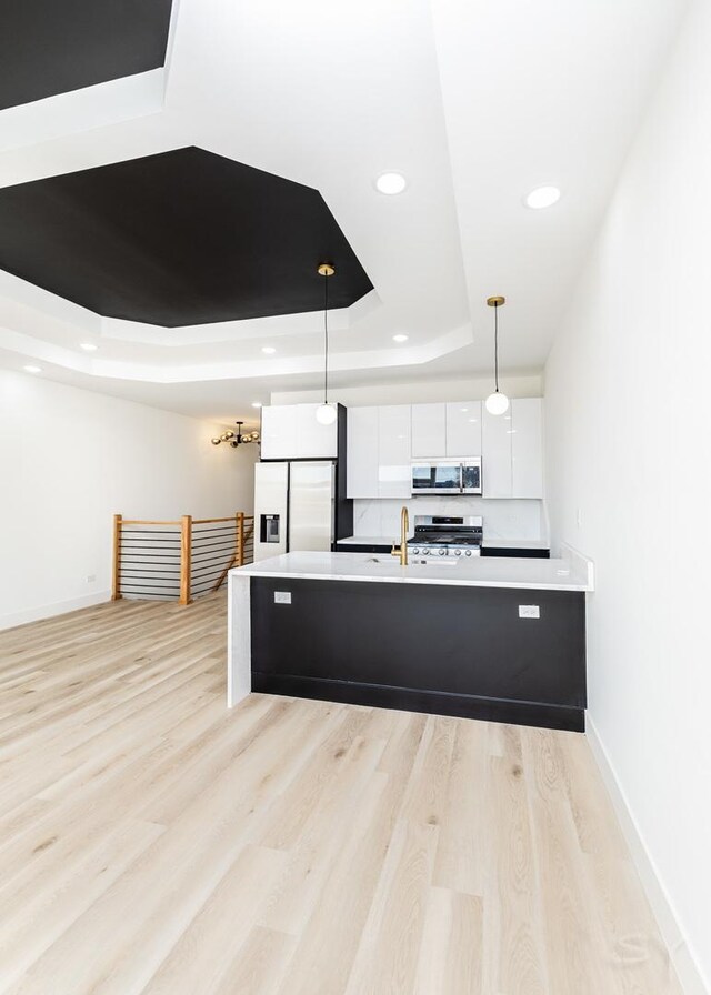 kitchen featuring a tray ceiling, light countertops, appliances with stainless steel finishes, white cabinets, and modern cabinets