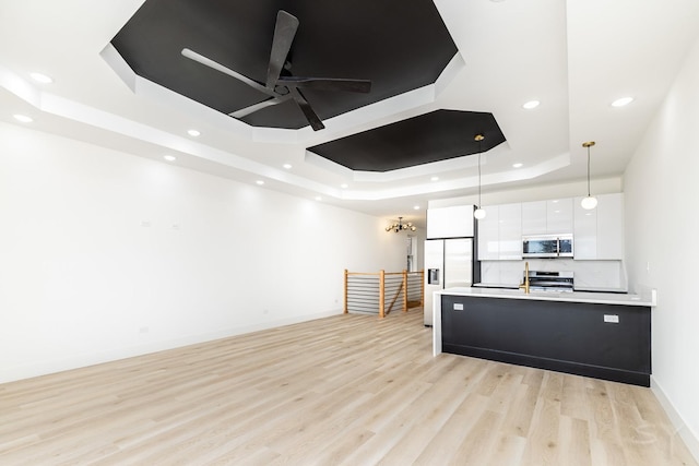 kitchen featuring pendant lighting, a raised ceiling, appliances with stainless steel finishes, white cabinetry, and modern cabinets