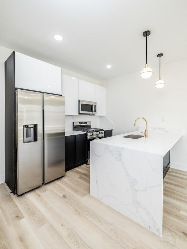 kitchen featuring light wood finished floors, stainless steel appliances, white cabinets, a sink, and a peninsula