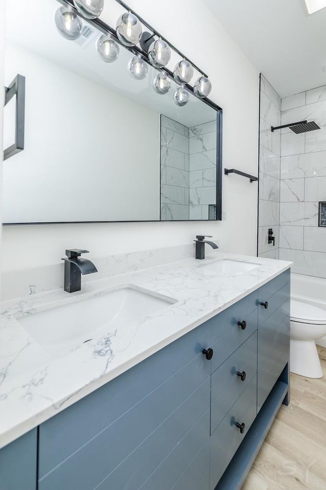 full bath featuring double vanity, toilet, a sink, and wood finished floors