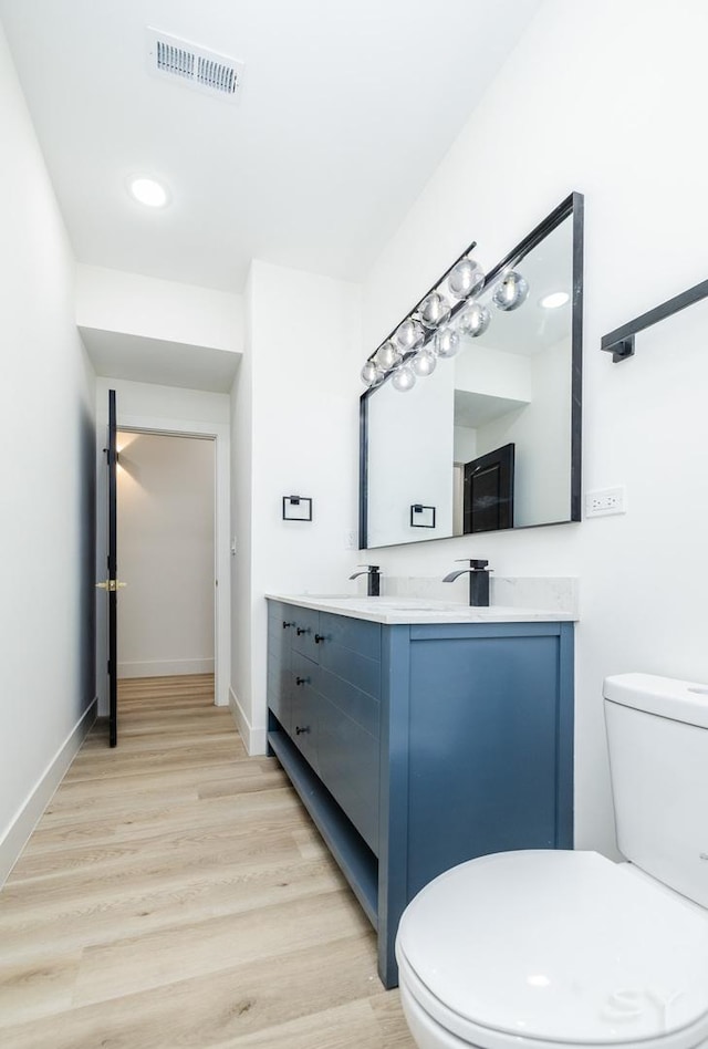 bathroom featuring baseboards, visible vents, toilet, wood finished floors, and vanity