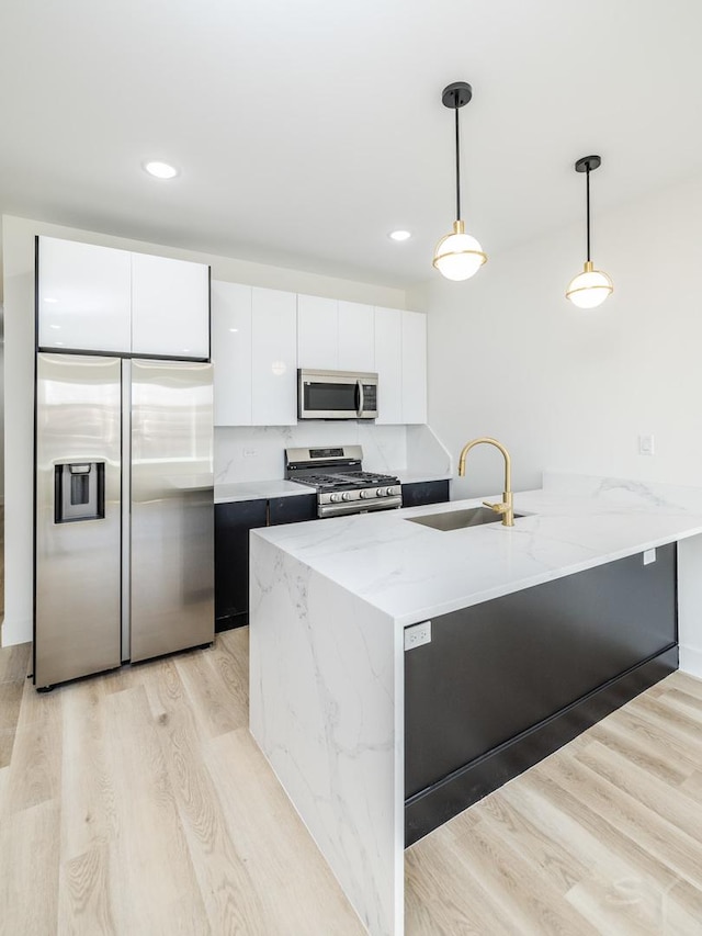 kitchen featuring stainless steel appliances, a peninsula, a sink, light wood-type flooring, and decorative light fixtures