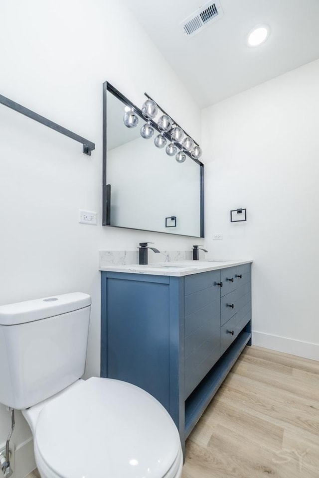 bathroom with double vanity, baseboards, visible vents, toilet, and wood finished floors