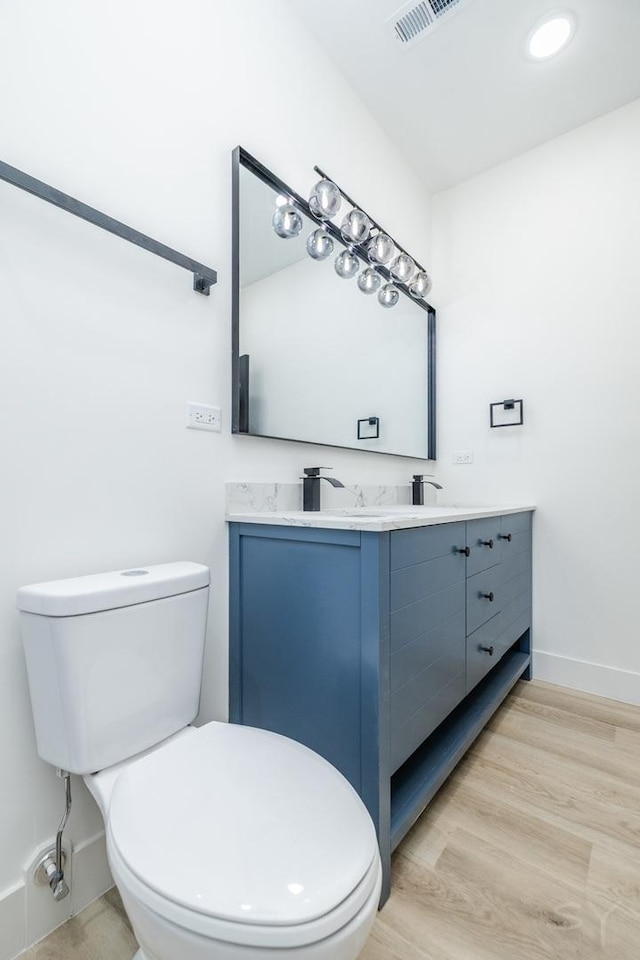 bathroom featuring toilet, wood finished floors, visible vents, baseboards, and double vanity