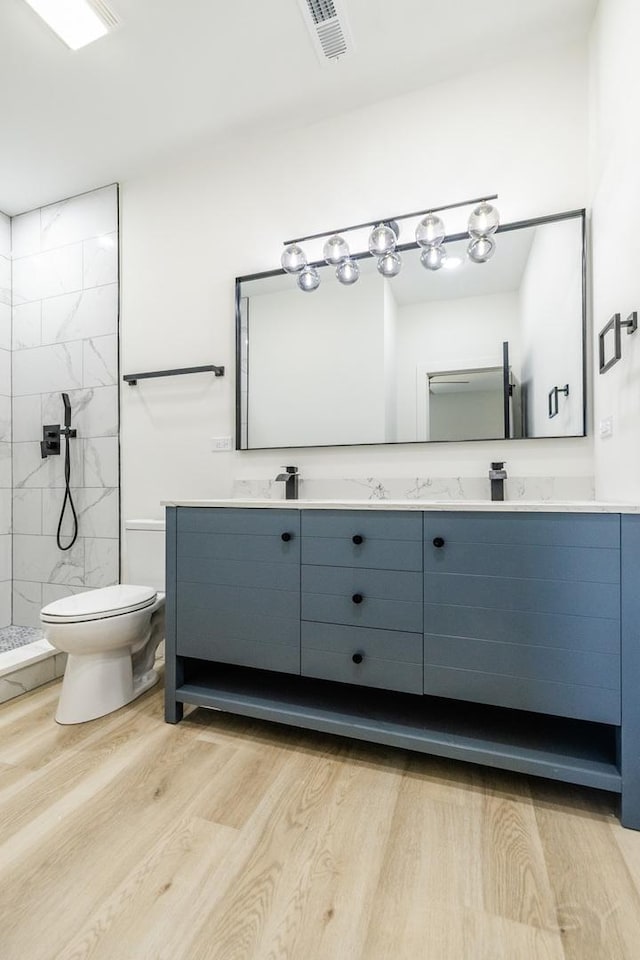 full bathroom with double vanity, visible vents, tiled shower, toilet, and wood finished floors