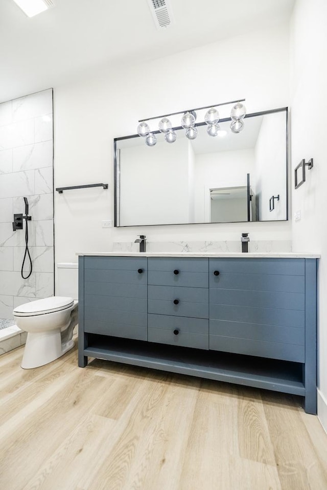 bathroom with visible vents, a tile shower, toilet, and double vanity