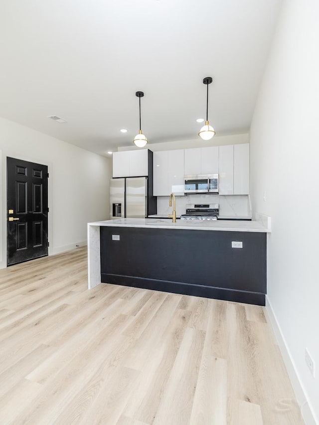 kitchen featuring appliances with stainless steel finishes, a peninsula, hanging light fixtures, light wood-type flooring, and white cabinetry