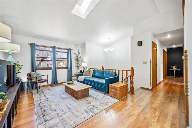 living area featuring light wood-type flooring, vaulted ceiling with skylight, and a chandelier