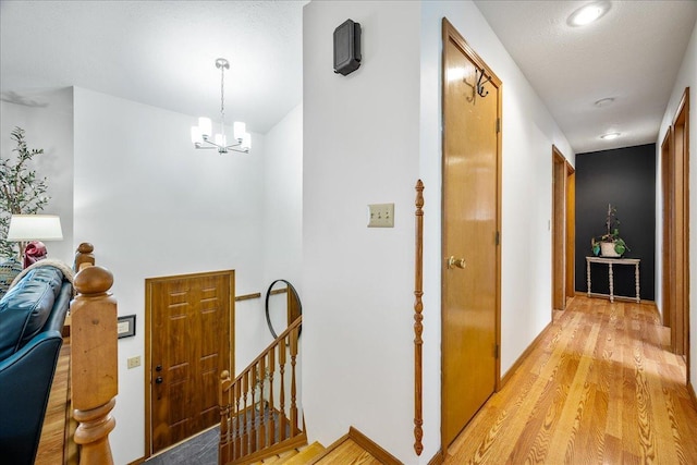 corridor featuring an upstairs landing, an inviting chandelier, and light wood-style flooring