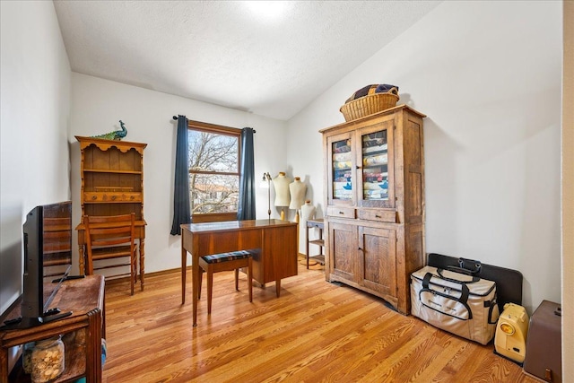 home office featuring a textured ceiling, light wood-style flooring, and vaulted ceiling