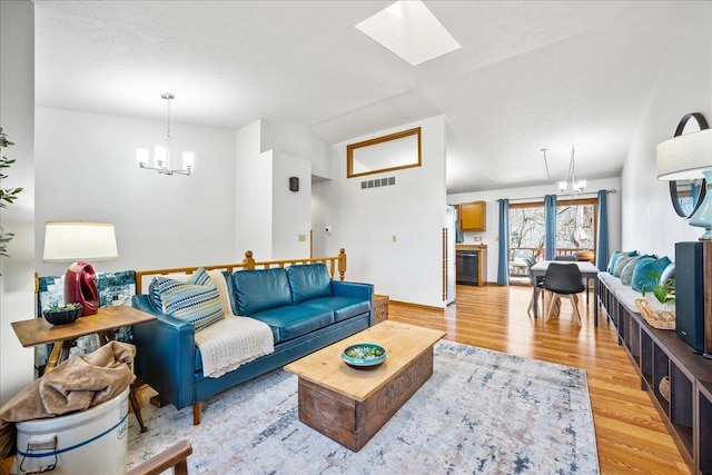 living area featuring lofted ceiling with skylight, light wood-style flooring, visible vents, and a chandelier