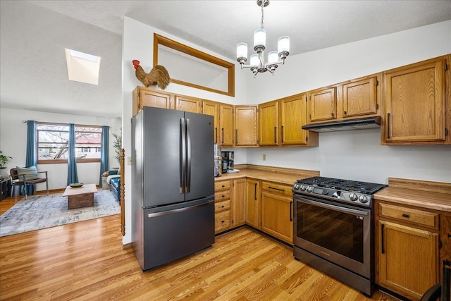 kitchen featuring under cabinet range hood, vaulted ceiling, light wood-style flooring, freestanding refrigerator, and stainless steel gas range