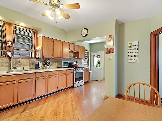 kitchen featuring decorative backsplash, gas range, light countertops, light wood-type flooring, and a sink