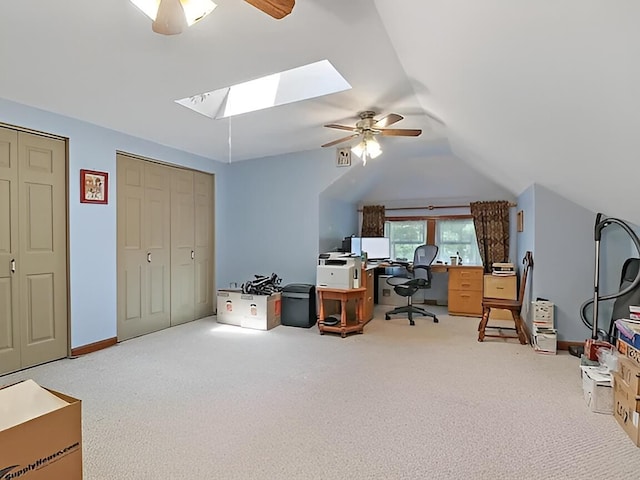 carpeted home office with vaulted ceiling with skylight, ceiling fan, and baseboards