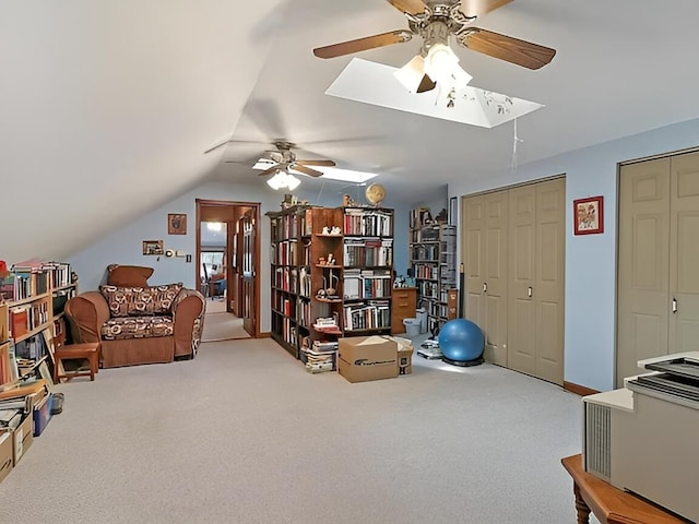 living area with baseboards, vaulted ceiling with skylight, a ceiling fan, and carpet flooring