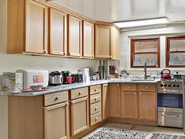 kitchen with stainless steel gas range, light brown cabinets, light countertops, and a sink