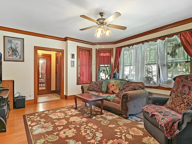 living area with ornamental molding, ceiling fan, baseboards, and wood finished floors