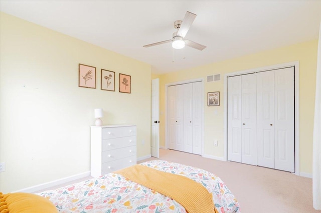 bedroom featuring visible vents, two closets, ceiling fan, baseboards, and light carpet