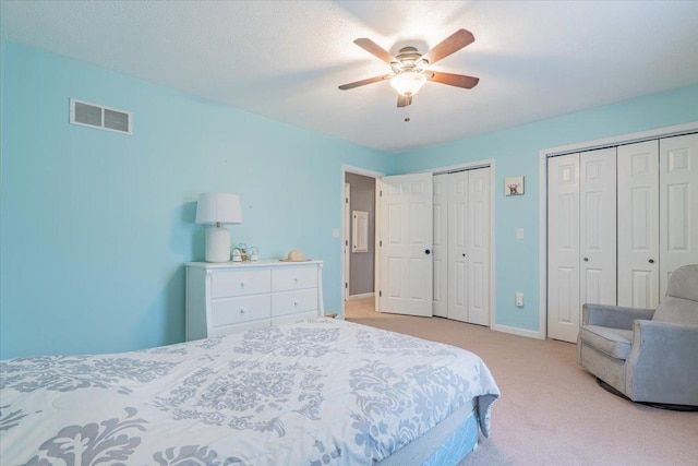 bedroom with visible vents, two closets, baseboards, light carpet, and a ceiling fan