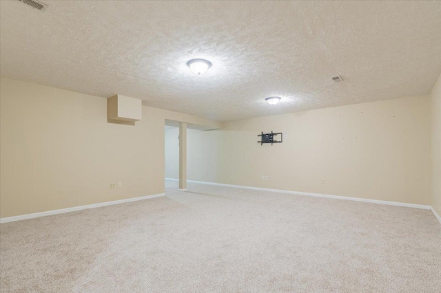 finished basement featuring light carpet, visible vents, a textured ceiling, and baseboards