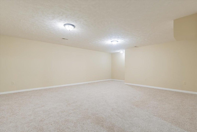 empty room featuring baseboards, light carpet, and a textured ceiling