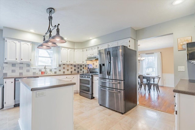 kitchen with under cabinet range hood, decorative backsplash, appliances with stainless steel finishes, and white cabinetry