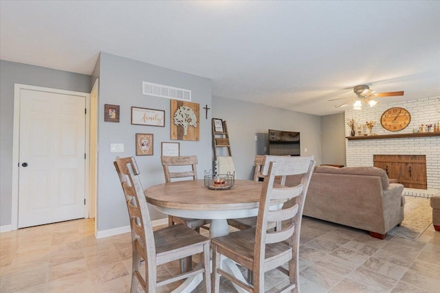 dining room featuring visible vents, brick wall, ceiling fan, baseboards, and a fireplace