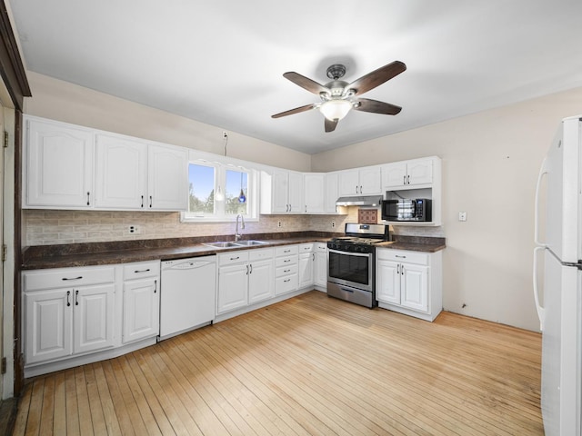 kitchen with white appliances, dark countertops, a sink, under cabinet range hood, and backsplash