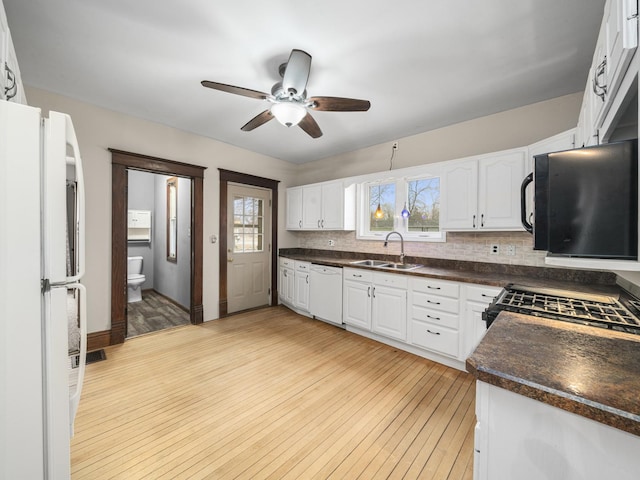 kitchen with white appliances, light wood finished floors, dark countertops, white cabinetry, and a sink