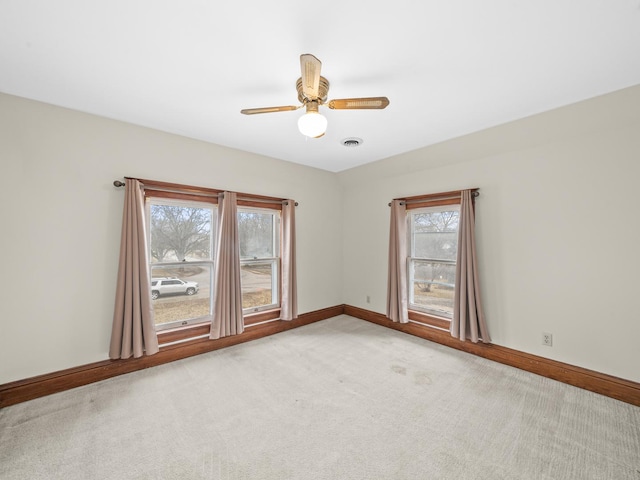 unfurnished room featuring light carpet, visible vents, a ceiling fan, and baseboards